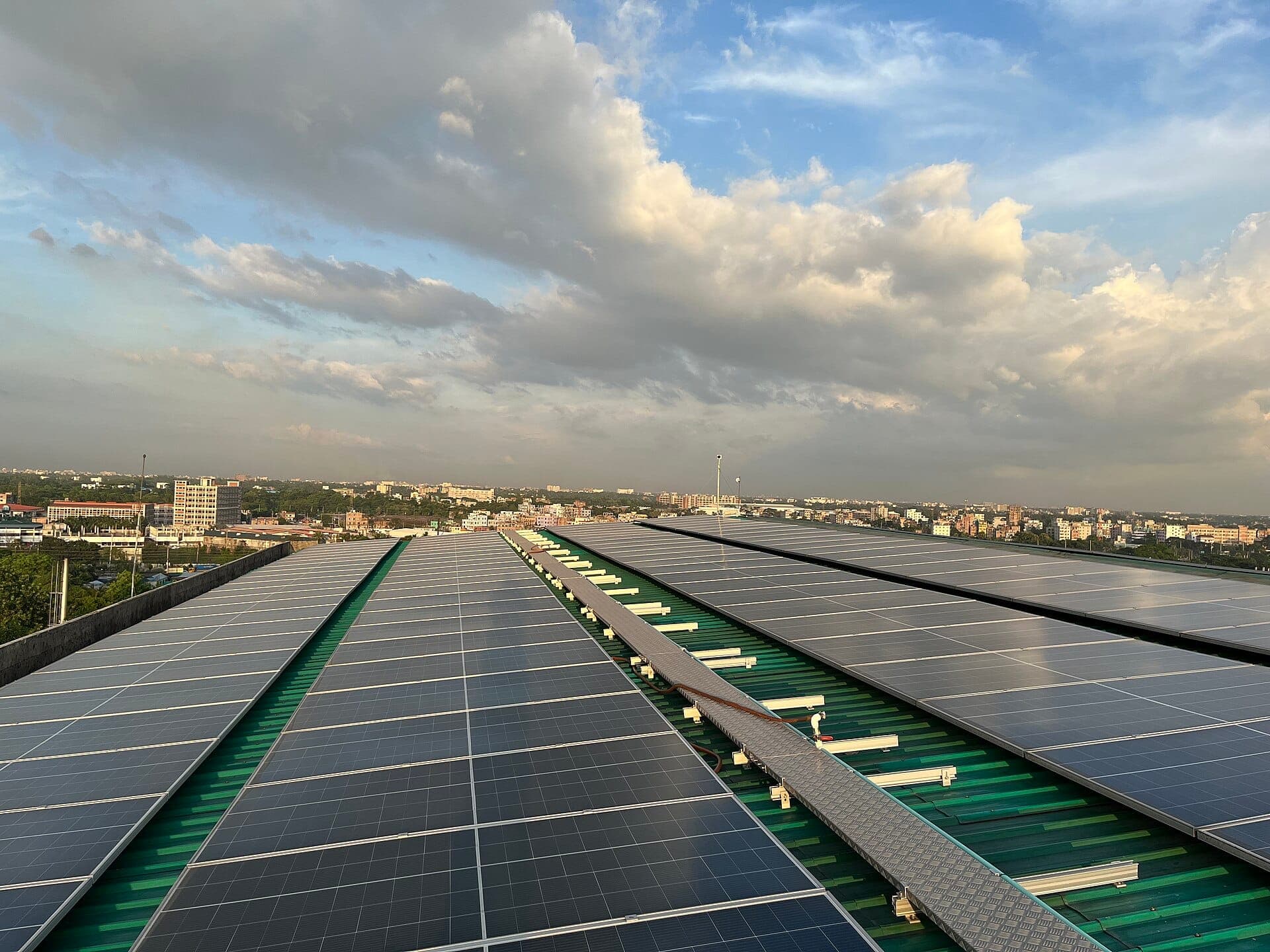 Rooftop solar panel array in greater Dhaka with the city skyline under afternoon clouds